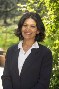Photo of Monisha Shah with a leafy green background.